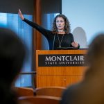 A professor gestures while speaking at a lectern.