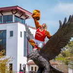 Vanessa Fingerlin atop a large bronze red hawk statue holding a costume head.