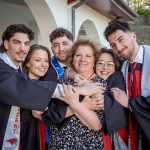 The Povolo quintuplets in graduation gowns surround and hug a smiling woman.