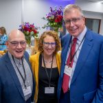 three people pose in front of flowers