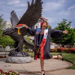 Graduate Iliana Woodhull celebrates in front of the Red Hawk statue.