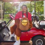 Aylin Alvarez-Santiago holds Ricky’s mascot head while seated in a red golf cart.