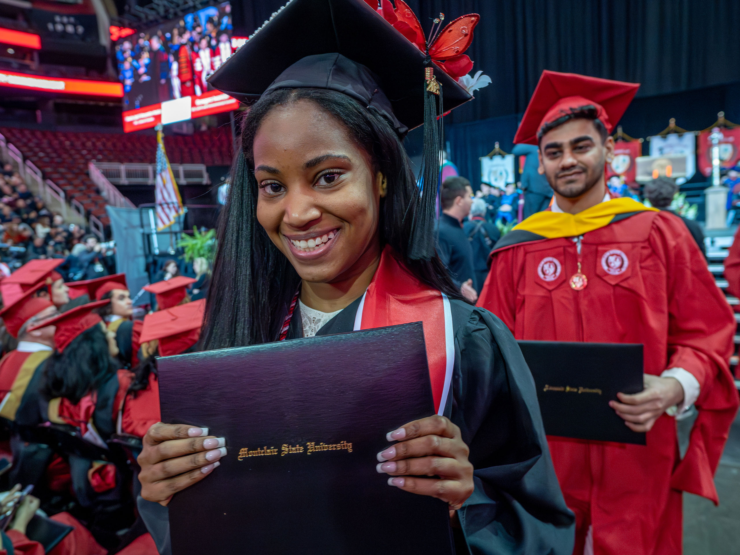 A graduate in a black gown proudly holds up her diploma.