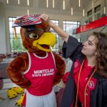 A student places a mortarboard on Rocky’s head.