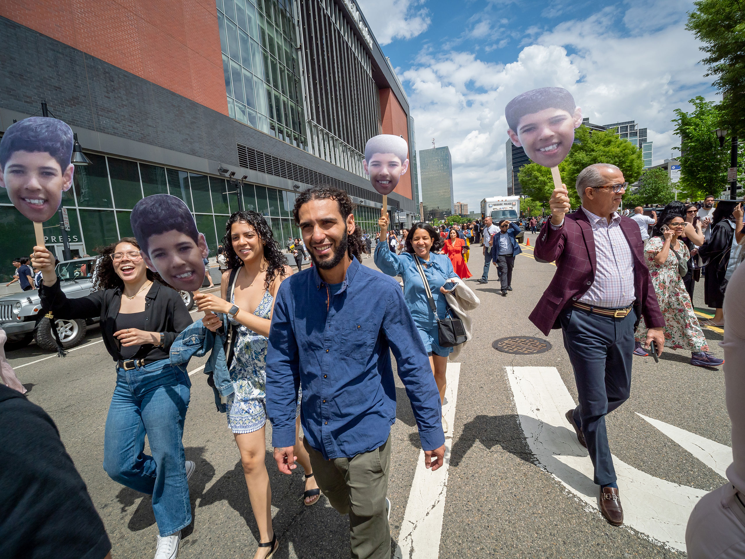 a graduate walking outside of prudential center flanked by family members holding up signs of their face.