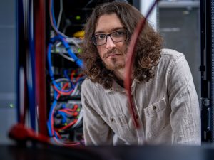 A photo of Joseph Quinn-Vitabile peering through networking cables at the University Hall data center.