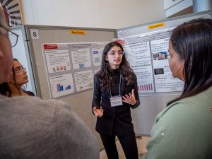 Melissa standing in front of a white board poster, presenting on her research.
