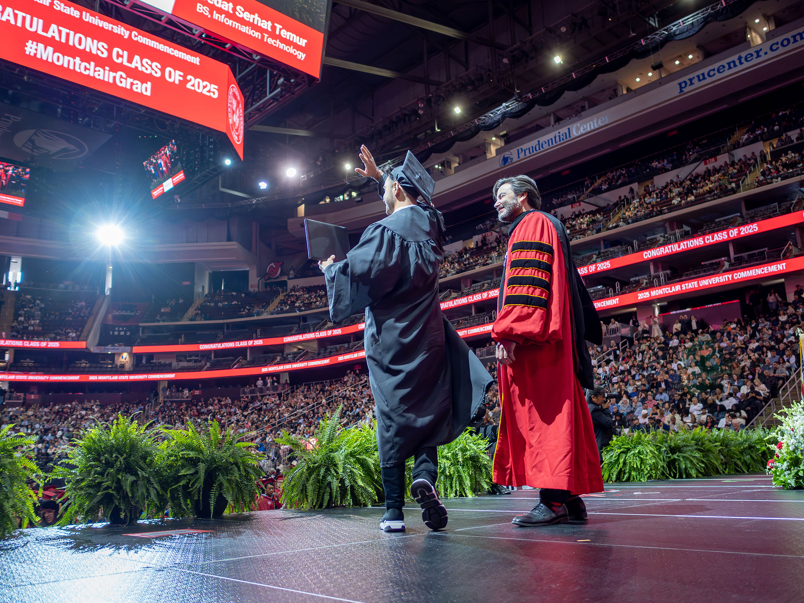 President Koppell stands next to a graduate waving on stage