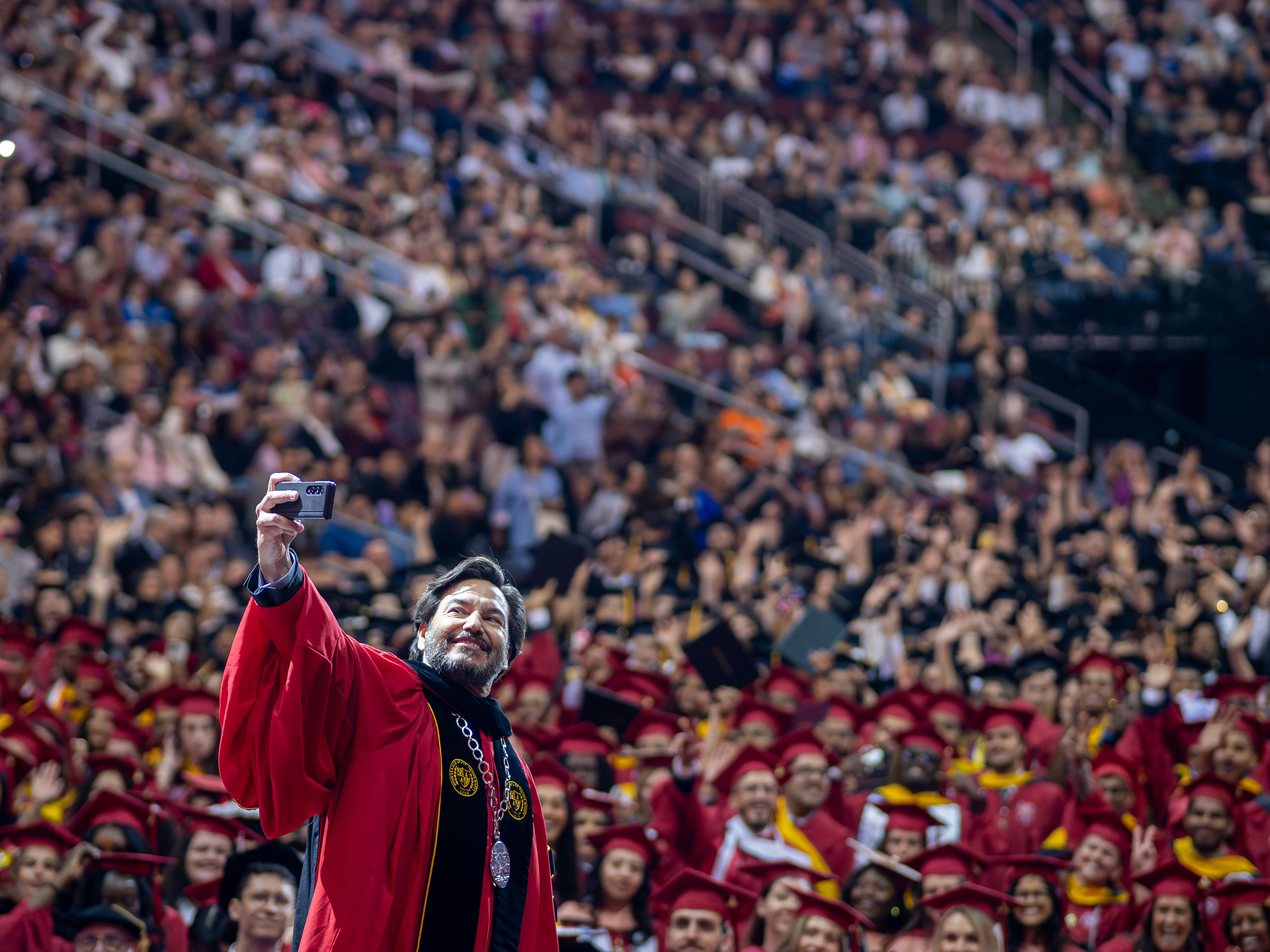 President Koppell taking a selfie from the stage with the crowd of seated graduates
