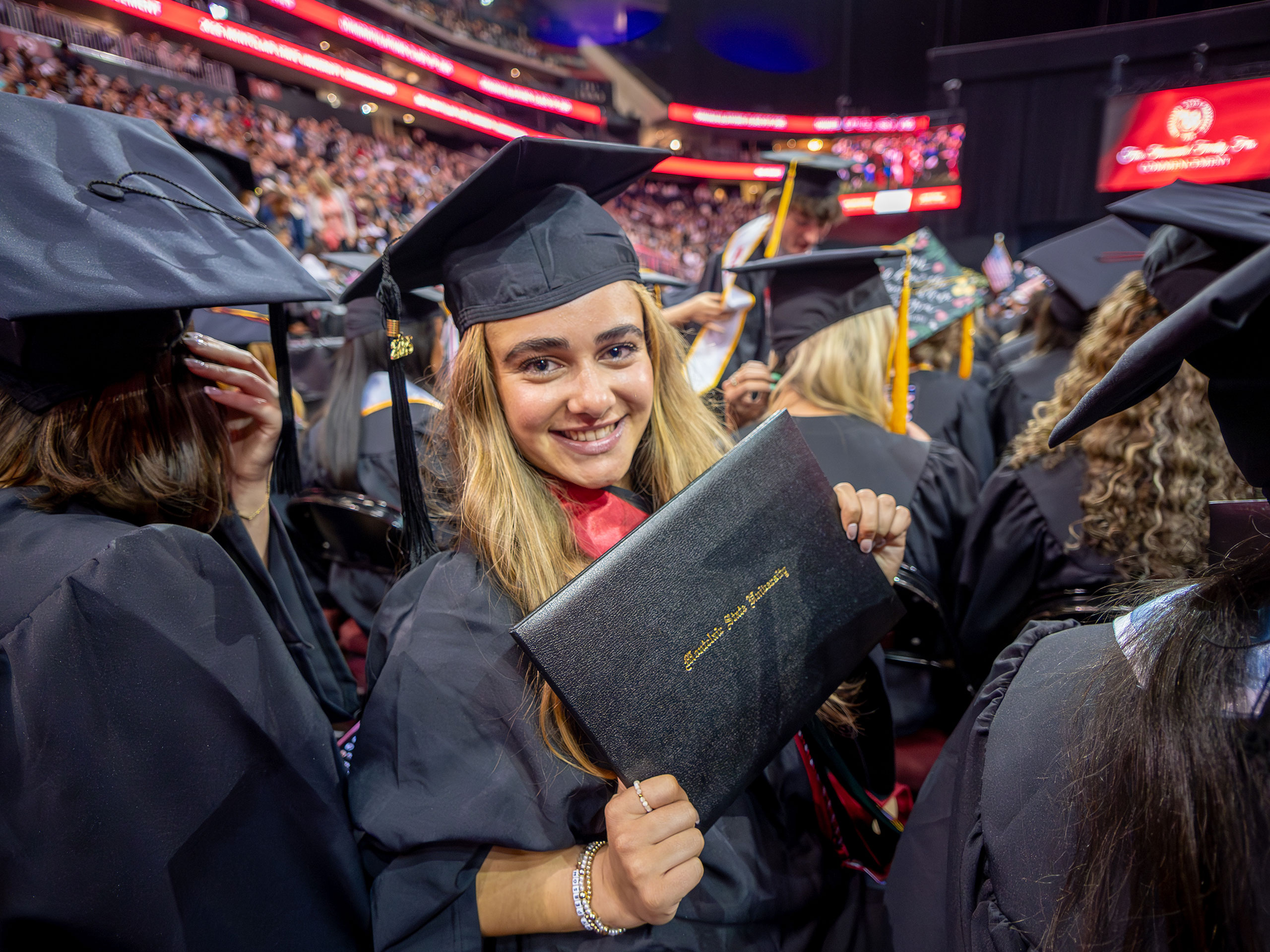 graduate in black cap and robe showing diploma holder