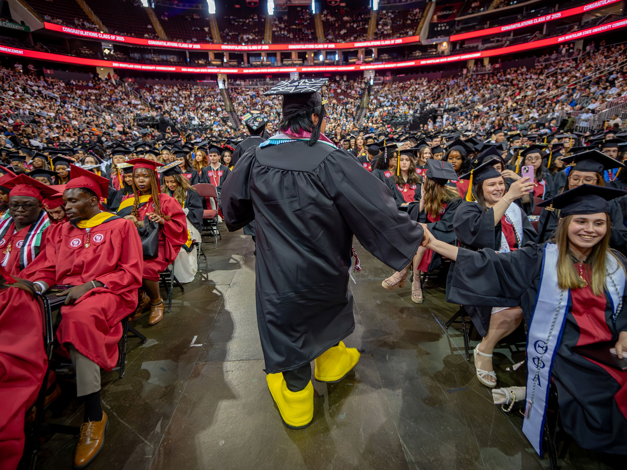 Graduate student walks down the aisle wearing the talons of Rocky, Montclair's mascot
