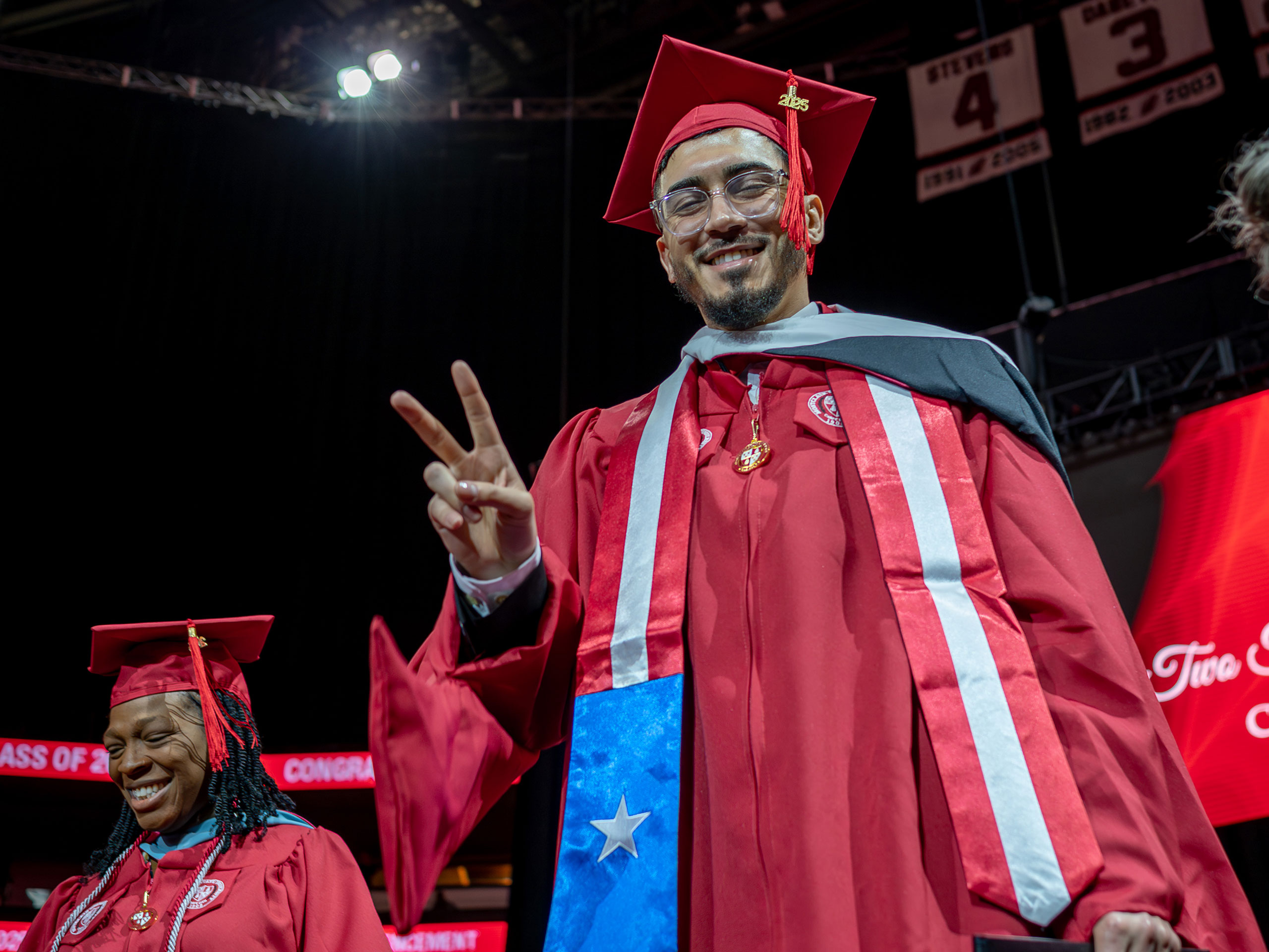 master's graduate in red cap and gown smiling and making a peace sign