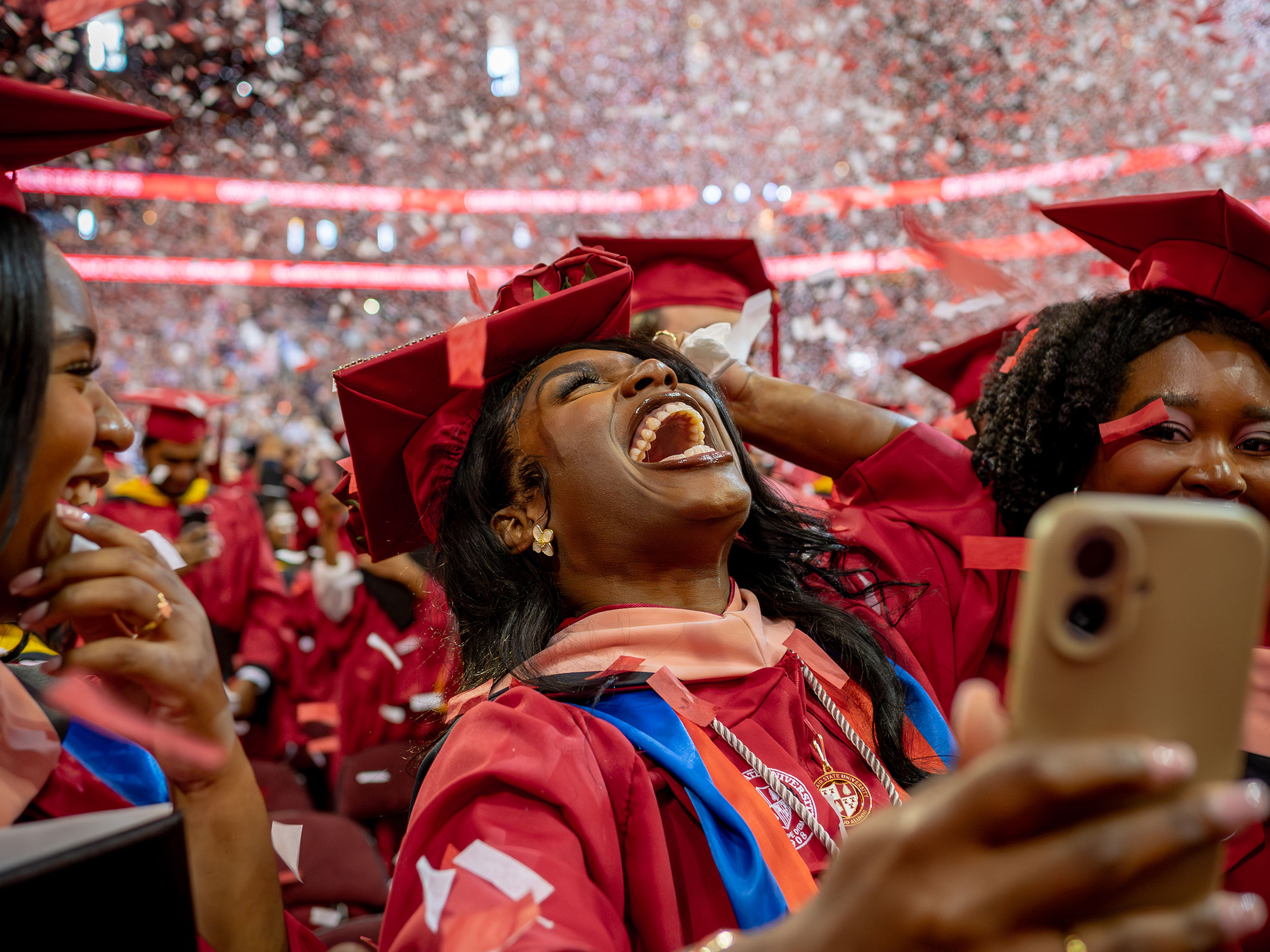master's graduate student in red cap and gown smiling with confetti falling around them