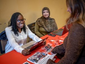 eema Dinnall, seated at a table with a laptop, talks with students about a career fair.