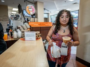 Sara Flores holds an iced coffee and a bag with a croissant sandwich at a Dunkin location on the Montclair campus.