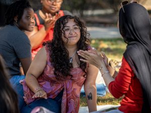 Sara Flores sits on a blanket outside, chatting with other students in a small group.