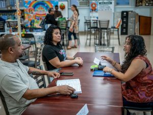 Sara Flores sits facing two adults in a classroom at Eastside High School, assisting them with English as part of the community-focused language program.