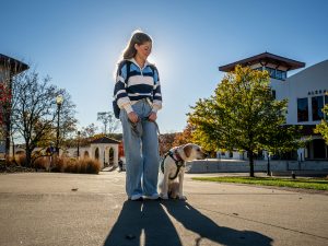 Makayla Snyder walks on campus with Katherine, her young yellow Labrador retriever in training, who wears a green “Seeing Eye Puppy” vest.