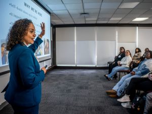 A speaker gestures as she addresses an audience of young women.