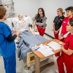 Nursing students gathered around medical manikin in simulation lab.