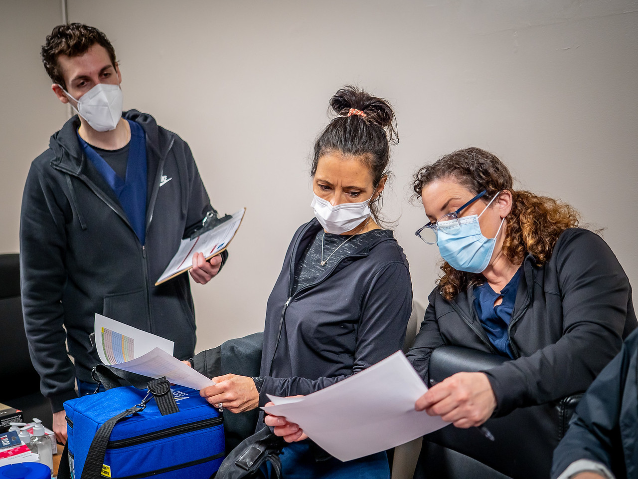 Three nurses standing and reviewing paperwork for vaccination efforts.
