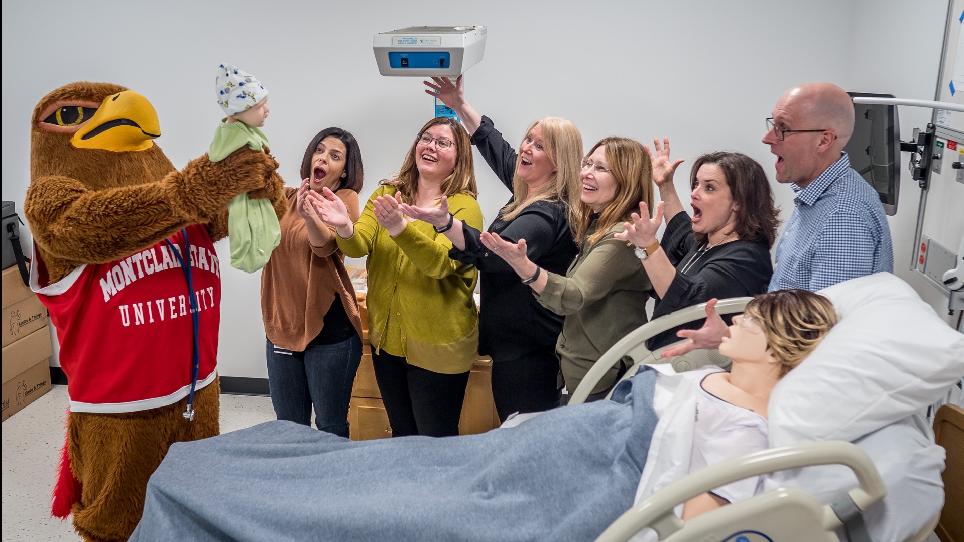 School of Nursing faculty and the school mascot, Rocky, "delivering" a baby in the Nursing Simulation Lab.