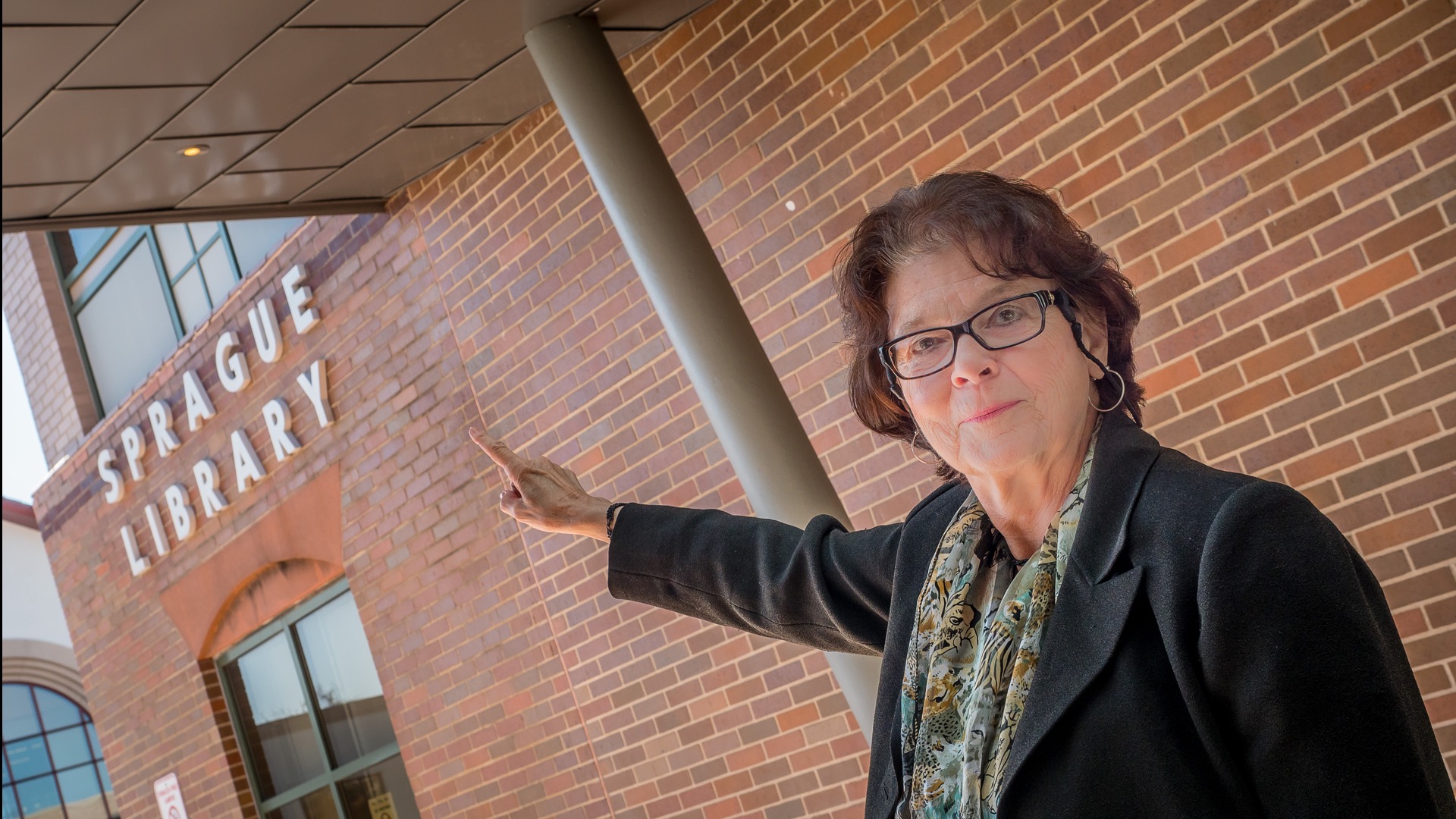 Dean of Library Services Judith Lin Hunt pointing to the exterior sign for Sprague Library.