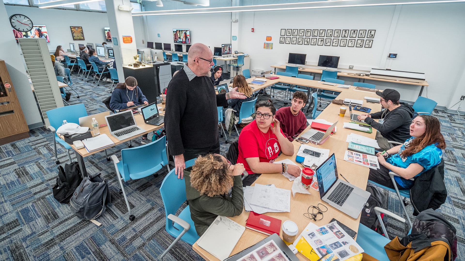 Visual Communication Design students and faculty conversing in a classroom.