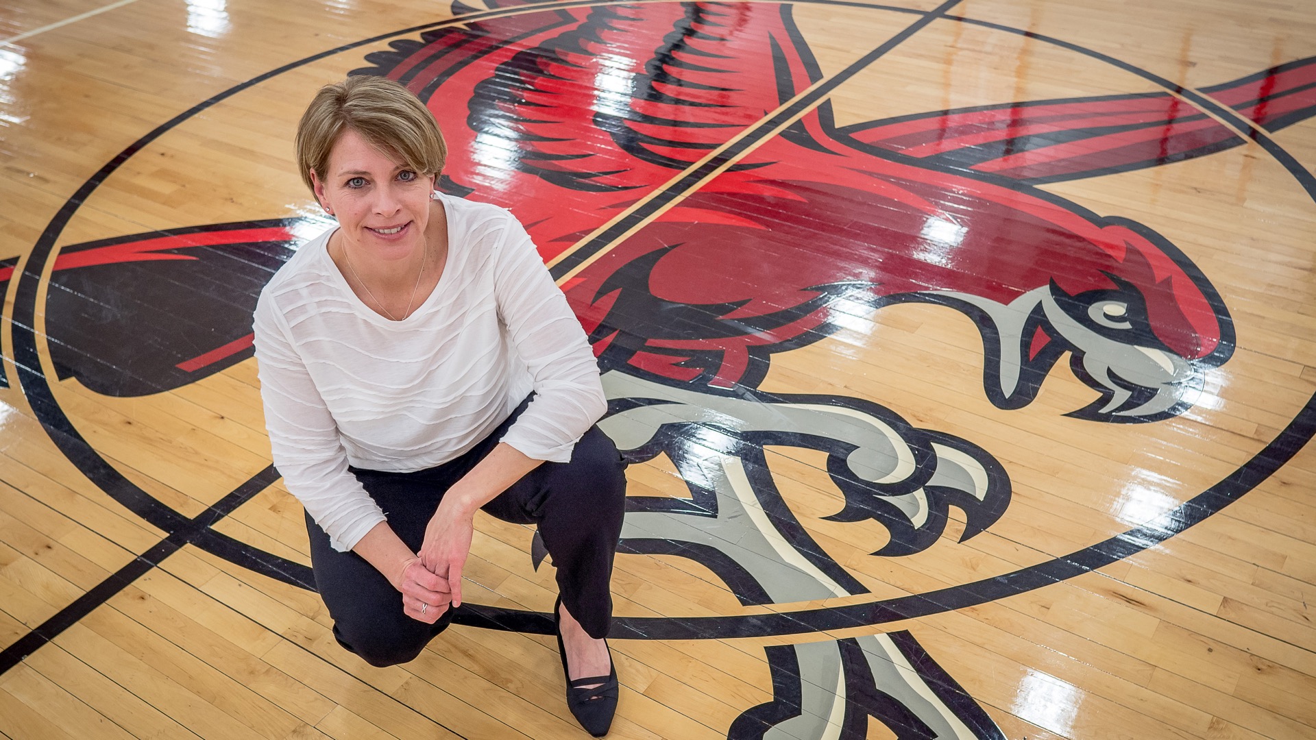 Women's basketball Head Coach Karin Harvey on the court with the Red Hawk mascot in the background.