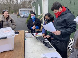Students  stand outside, masked, sorting and scanning documents
