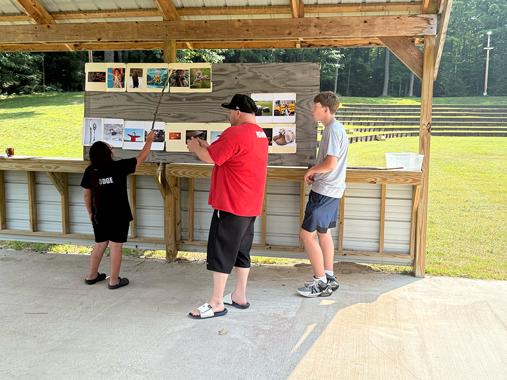 two adults and one child stand looking at a board with pictures of objects at Munsee Language Camp