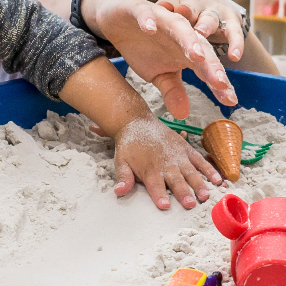 Child's and adult's hands playing in sandbox