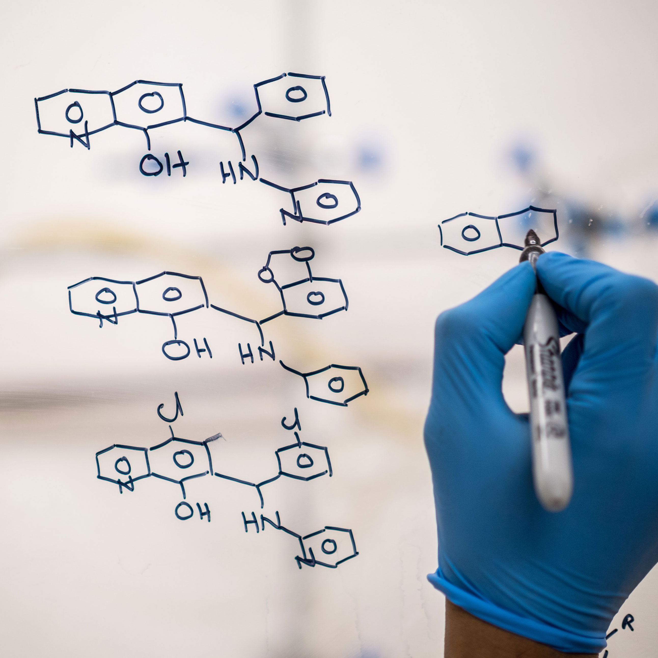 Person's hand writing chemical formula with sharpie on glass pane in lab