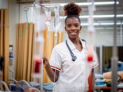 Nursing student smiling at the camera. Her hand is holding onto an IV Pole with two bags attached.