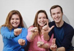Photo of three students holding up their hands to sign ASL