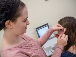 Photo of an audiology student fitting a hearing aid