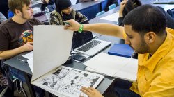 Student flipping through sketch pad revealing inked comic book style pages