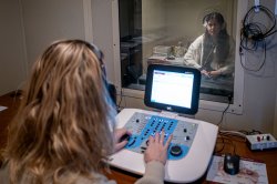 student at a control panel observing a person wearing headphones through window