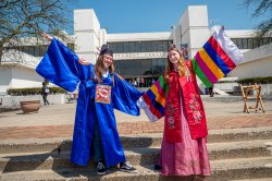 Two students wearing colorful traditional Korean hanbok and robes posing with arms outstretched in front of the Student Center