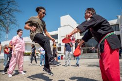 Student practices a high kick during a taekwondo demonstration outdoors at a campus event.