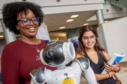 Two young women smiling at symposium as they check out a presentation on robotics