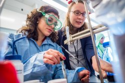 Professor looks over student's shoulder as she handles chemicals at a workbench using a pipette