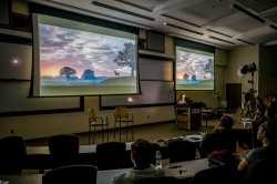 Students watch a film on projector screens in a darkened lecture hall