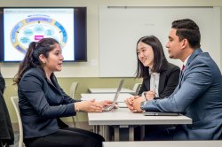 One student with a laptop sits on one side of a table while two others sit across from her, as if in an interview.