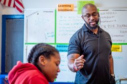 An elementary school teacher speaks to a class as they complete an assignment.