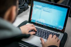 Over-the-shoulder view of a student using a laptop to write an Android app in Java
