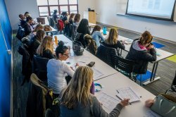 Students at tables in two rows in a brightly lit classroom