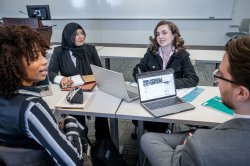 Students in conversation, sitting around table with laptops and notebooks