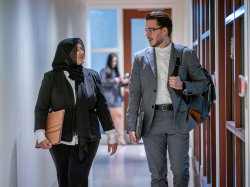 Two students in business attire, walking and talking in a hallway