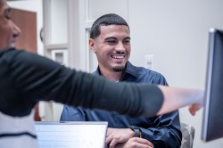 Two students smile as they look at a computer monitor.
